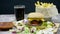 Shot of burger, french fries, cola and ketchup on wooden table over black background