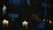 Shot capturing a priest sitting at the table, surrounded by candles, crosses and beads, holding a book in hands, reading