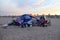 A shot of a colored homeless encampment on the beach with silky brown sand, people relaxing and powerful clouds at sunset