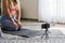 Shot of fitness woman sitting on yoga mat and using mobile phone. Fit young woman using cellphone while doing exercise at home.