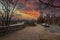 A shot of a long sidewalk with red brick with gorgeous autumn trees and parked cars along the street with powerful clouds