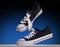 Shot a pair of classic black and white sneakers levitating in air with tie their laces on a dark blu background with copy
