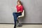 shot of pretty serious blonde woman focused in laptop computer, sits at white armchair, dressed in red jumper and jeans,