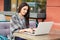 Shot of serious brunette young female student prepares for studying seminar, keyboards on laptop computer, wrapped in coverlet, si