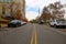 A shot of a street with a yellow line in the center with parked cars along the street and gorgeous autumn colored trees