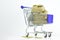 Shot of a tiny sack of golden coins in a shopping cart with a silver trinket on a white background