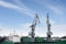 Shot of two old, rusty, grey port cranes with big hooks, lifting cargo in ship on clear blue sky background.