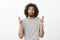 Shot of worried handsome bearded Eastern male model with afro hairstyle in striped t-shirt, raising crossed fingers and