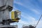 Shot of yellow control cabin with worker. Old, rusty, grey port crane lifting cargo in ship on clear blue sky background.