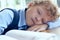 Shot of a young curly boy sleeping during the lesson at elementary school.