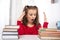 A shot of a young girl sitting at a table with two large stacks of books and emotionally experiencing stress from the fact that