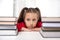 Shot of young girl   sitting at  the table with two large stacks of books and   looking dreamily into the distance