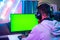 shoulder shot of professional gamer playing live video game on green screen monitor by talkng on headphones - concept of