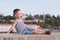 Shouting little boy in shorts and singlet sitting on port buildings background