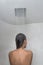 Shower woman showering relaxing under rain water falling from rainfall showerhead in hot shower. Young adult from behind