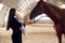 Showing the animal. Mother with baby on the hands is standing indoors with horse in hangar