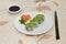 Shrimp and avocado rolls on a white plate with salmon decoration, soy sauce and black chopsticks in rustic table.