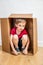 Shy boy hiding in cardboard box playing in new home