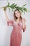 Shy caucasian girl with big eyes stands in a velvet pink dress and holds a white Lily in her hand as a symbol of innocence and pur