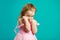 Shy little girl presses her hands to face and hides countenance, portrait of cute child on blue isolated background.