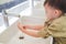Sian 3 - 4 years old toddler baby boy child washing hands by himself on sink and water drop from faucet in public toilet