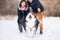 Siberian husky runs in front of a couple walking in a winter park