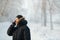 Siberian man talking on the phone outdoors by cold day in a warm winter down jacket with fur hood. Snow frost