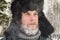 Siberian Russian man with a beard in hoarfrost in freezing cold in the winter freezes and wears a hat with a earflap