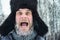 Siberian Russian man with a beard in hoarfrost in freezing cold in the winter freezes and wears a hat with a earflap