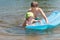 Sibling children having fun with inflatable blue pool lilo in summer lake outdoor