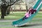 Sibling children sliding down on old park playground slide at blooming spring fruit tree background