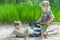 Sibling girl and boy digging on beach dune and burying each other in white sand at pinewood background