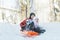 Siblings having downhill fun on winter plastic snow slider outdoors