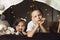 Siblings lie in a hut of chairs and blankets. Brother and sister smiling playing at home