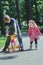 Siblings playing with pink and yellow kids tricycle on park tarmac footpath