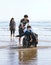 Siblings walking disabled brother in wheelchair in water along beach