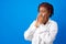 Sick afro woman sneezing in paper napkin against blue background