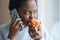 Sick afro woman trying to sense smell of half fresh tangerine orange talking on phone. Covid-19