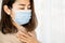 Sick Asian woman wearing face mask having sore throat from cold and flu standing next to the windows