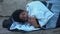 Sick black teenager shivering cold covering by sleeping bag lying street poverty