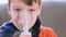 Sick blond boy inhaling through inhaler mask, close-up face. Use nebulizer and inhaler for the treatment.