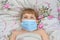 A sick child lies in bed wearing a medical mask