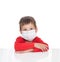 The sick five-year-old boy sits at a white table with medicine healthcare mask for is protection again virus