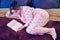 A sick flu woman lies on a bed and reads a book in quarantine. Red-haired girl in pajamas on the bed reading a book