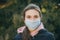 Sick girl wearing protection during pandemic. Pretty young Caucasian girl taking on medical mask outdoor. Girl Wearing