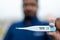 Sick man holds digital thermometer with body temperature reading in Fahrenheit up close to the camera