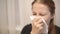 A sick middle-aged woman sneezes and blows her nose in a handkerchief.