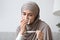 Sick muslim woman in hijab sitting on sofa looking at thermometer