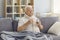 Sick senior man with a glass of water in his hand suffers from a severe cold sitting on the couch.