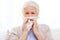 Sick senior woman blowing nose to paper napkin